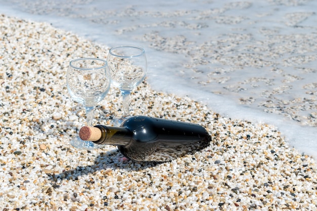 Fles rode wijn met wijnglazen op het strand in de zomer