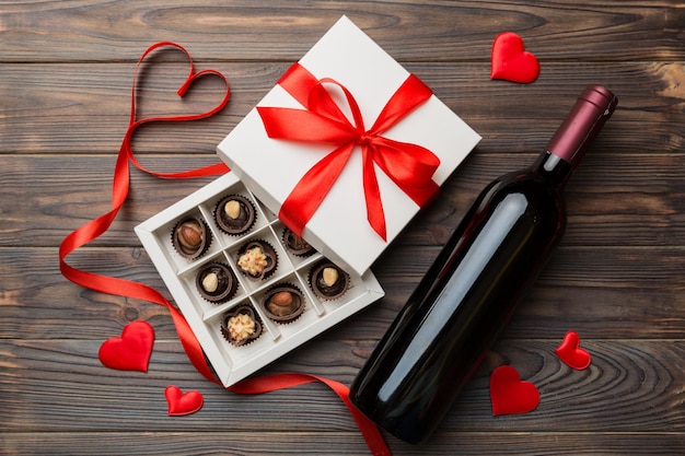 Fles rode wijn op gekleurde achtergrond voor valentijnsdag met cadeau en chocolade. hartvormig met geschenkdoos chocolaatjes bovenaanzicht met kopieerruimte