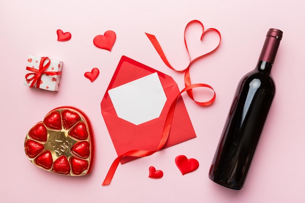 Fles rode wijn op gekleurde achtergrond voor Valentijnsdag met geschenkdoos, envelop en chocolade. Hartvormig met geschenkdoos chocolaatjes bovenaanzicht met kopieerruimte.