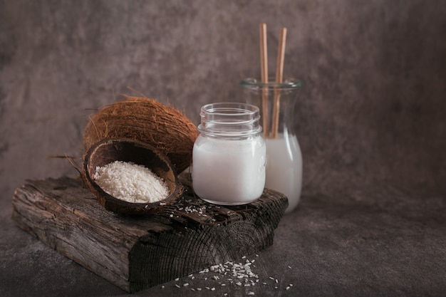 Fles veganistische kokosmelk, kokosolie, hele kokosnoot en vlokken op donker