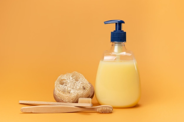 Fles vloeibare zeep geel en bamboe tandenborstels met een spons gemaakt van natuurlijk materiaal op een beige achtergrond Clean hands concept Shampoo Vloeibare zeep Aromatisch badzout en andere toiletartikelen