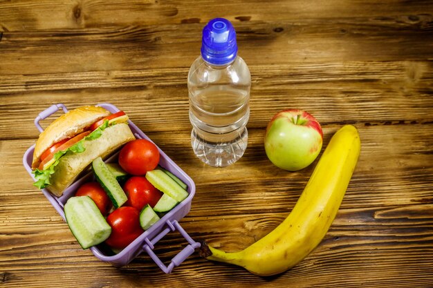 Fles water appel banaan en lunchbox met hamburgers en verse groenten op een houten tafel