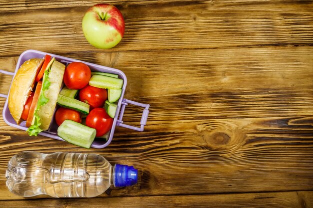 Fles water appel en lunchbox met hamburgers en verse groenten op een houten tafel Bovenaanzicht kopieerruimte