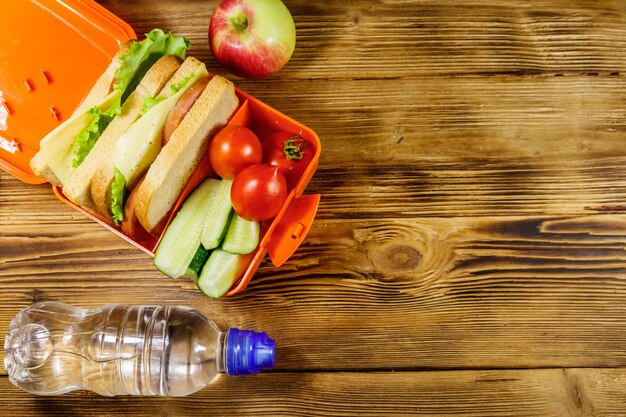 Fles water appel en lunchbox met sandwiches en verse groenten op een houten tafel Bovenaanzicht kopieerruimte