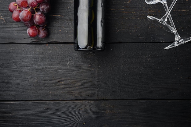 Fles wijn en glas rode wijn met rijpe druiven set, op zwarte houten tafel achtergrond, bovenaanzicht plat lag, met kopie ruimte voor tekst