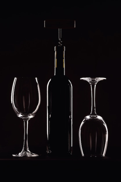 Fles wijn met een glas op een zwarte achtergrond, kurkentrekker