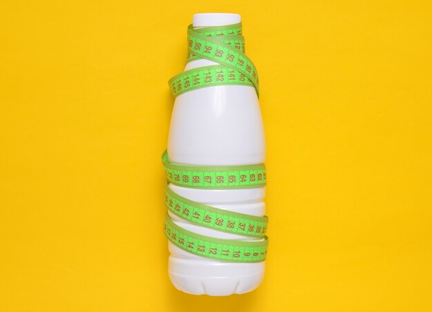 Fles yoghurt verpakt in een liniaal op een gele achtergrond