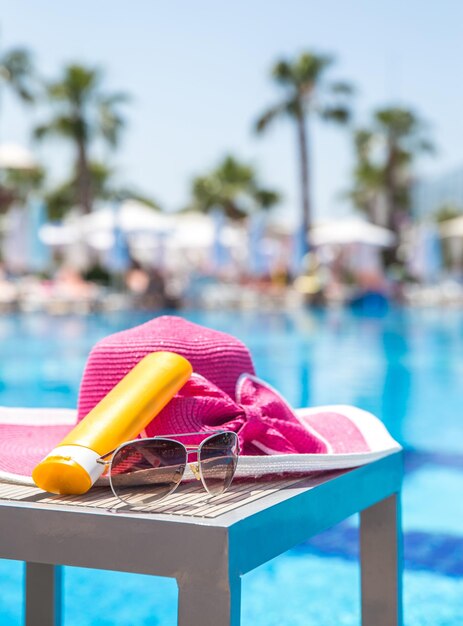 Fles zonnebrandcrème hoed en zonnebril naast zwembad in hotel