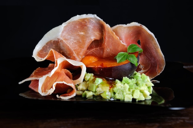 Foto avocado in carne con una fetta di albicocche nere con salsa piccante dolce e piccante e prosciutto di parma