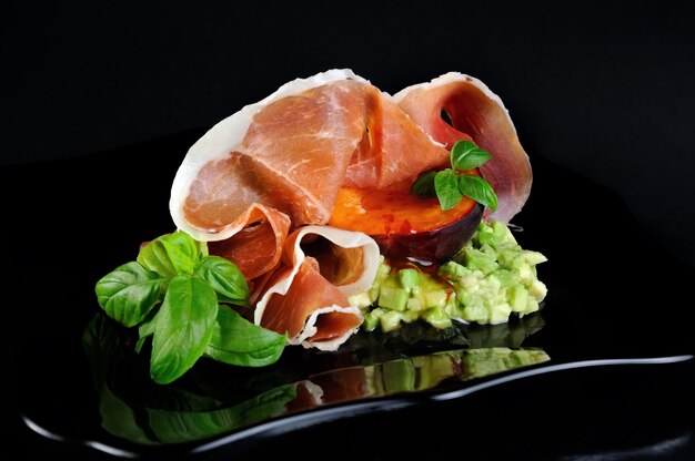 Flesh avocado with a slice of black apricots with spicy hot and sweet sauce and Parma ham