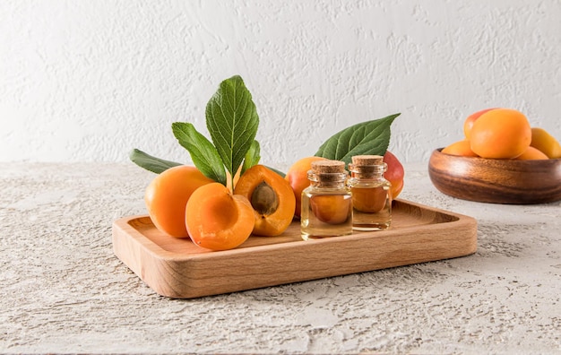 Flessen abrikozenolie op een houten dienblad tussen rijpe abrikozen rustgevende verzorging huidherstel grijze cementachtergrond