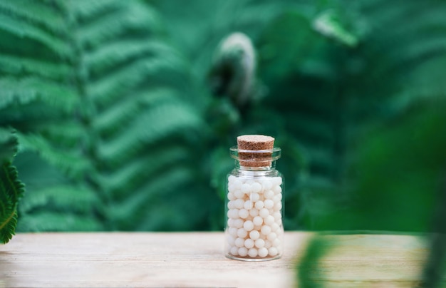 Flessen homeopathische bolletjes op groene varenachtergrond. Homeopathie geneeskunde.