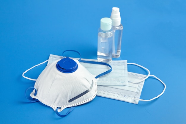 Flessen met antibacterieel handdesinfecterend middel en chirurgische maskers op blauwe achtergrond