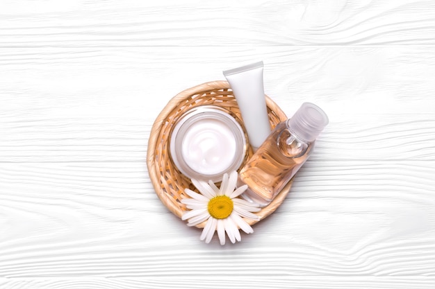 Flessen met cosmetica en kamillebloemen in een rieten mand. Crème, tonic, water en gezichtsscrub. Witte buizen. Mockup natuurlijke cosmetische producten.