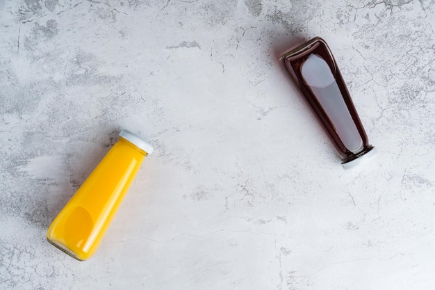Flessen met gele en rode vloeibare halthy drank op grijze achtergrond Sinaasappel- en kersensap