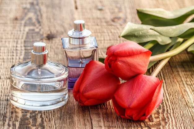 Flessen parfum op houten planken met rode tulpen.