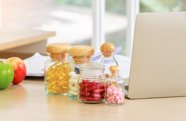 Flessen pillen, capsules en vitamines met notebookcomputer en vers fruit op het bureau van de voedingsdeskundige