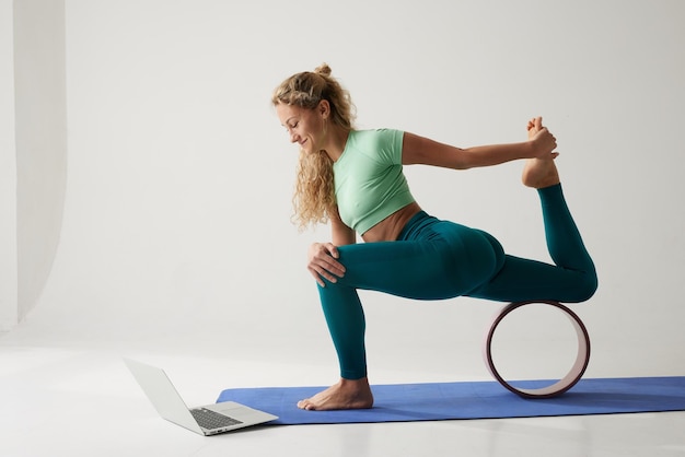 flexibel jong meisje doet gymnastiek flexibiliteit en strekken met behulp van een yoga wiel online op een witte achtergrond