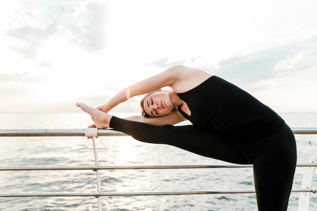 Flexibele vrouw doet yoga asana in de buurt van de zee op zonsopgang in de ochtend, het beoefenen van sport en fitness oefeningen
