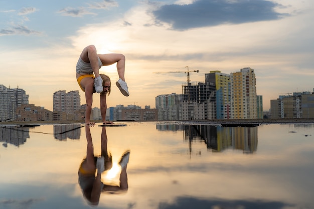 Flexibele vrouwelijke turnster die handstand en gymnastiek doet met weerspiegeling in het water op stadsgezichtba...