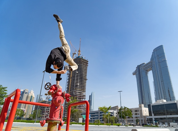 유연한 Acrobat은 흐린 두바이 도시 풍경으로 소방 소화전에서 한 손으로 균형을 유지합니다.