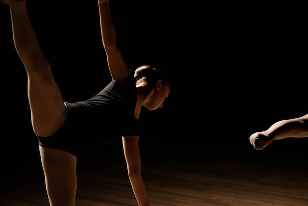 Flexible ballerinas stretch on a dark lighted scene