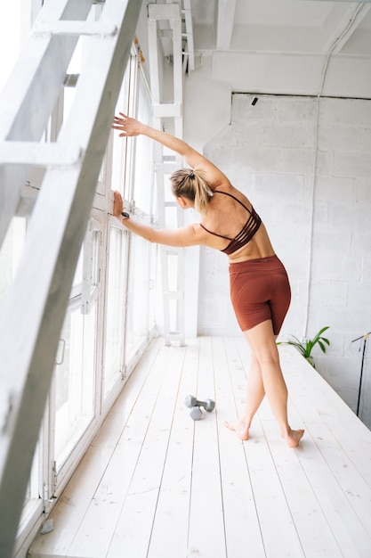 Giovane donna in forma flessibile con un corpo atletico perfetto che indossa abbigliamento sportivo facendo esercizi di stretching