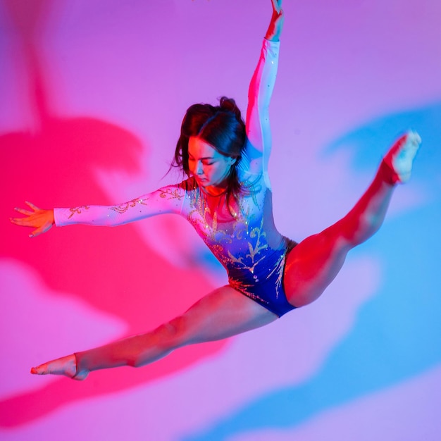 Гибкая девушка артистка художественной гимнастики прыгает на белом темном фоне грациозность в движении