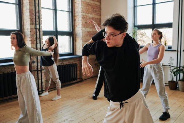 Flexible teenage guy in black sweatshirt and white pants\
training in dance hall