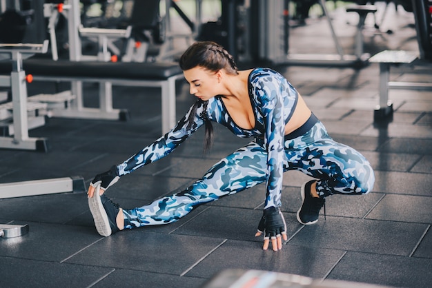 Giovane femmina flessibile che allunga la sua gamba destra in palestra. uno stile di vita sano. concetto di fitness. copyspace