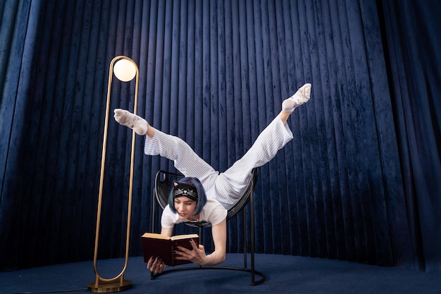 Flexible young girl in pajamas reading book in a creative way indoor  concept of individuality studying and selfdevelopment