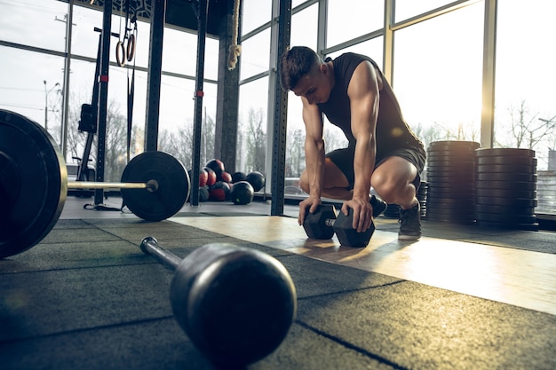 Flexible. Young muscular caucasian athlete training in gym, doing strength exercises, practicing, work on his upper body with weights rolling. Fitness, wellness, sport, healthy lifestyle concept.