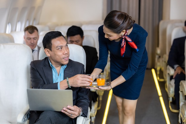 Flight attendant serving, Asian female flight attendant serving drink to passengers on airplane, Cabin crew or air hostess working in airplane.