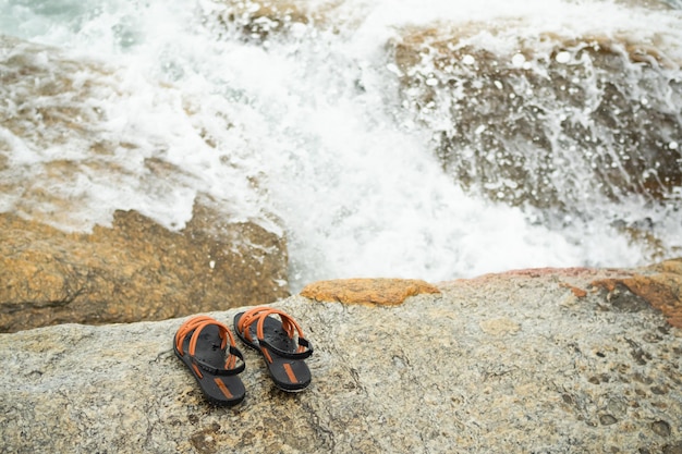 Flip flop on stone with splash wave white water at coast of sea oceantourist tropical vacation travel summer holidays nature seaside concept woman sandals on rock