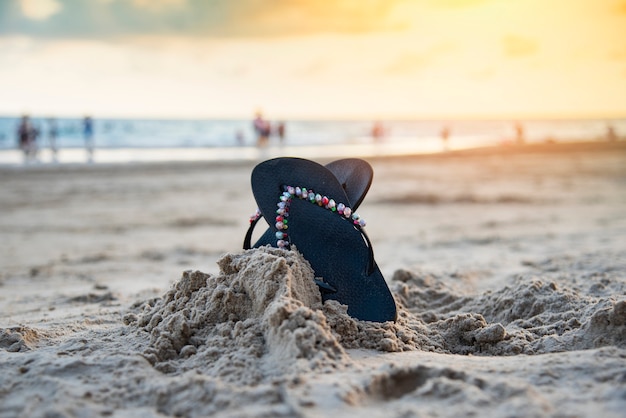 Flip-flop sulla spiaggia con il tramonto della spiaggia sabbiosa e fondo del mare dell'oceano