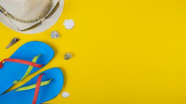 Flip-flops, hat, sunglasses and seashells on yellow background. top view