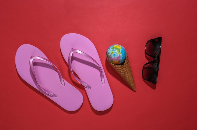 Flip flops, ijs wafel kegel met globe, zonnebril op rode achtergrond.