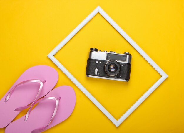 Flip flops and retro camera on yellow surface with white frame