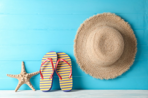 Flip-flop, cappello di paglia e stelle marine sulla tavola bianca contro il fondo di legno di colore, spazio per testo. concetto di vacanze estive