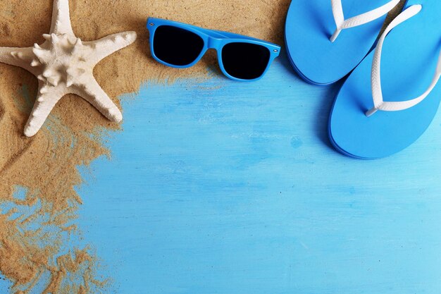 Flip flops and sunglasses with sand on wooden background