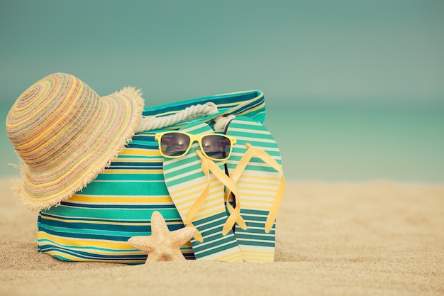 Flipflops and bag on sandy beach against blue sea