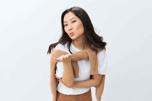 Flirting happy lovely korean young female in beige warm sweater\
sending kiss at camera posing isolated on over white studio\
background the best offer for ad autumn style concept seasonal\
sale