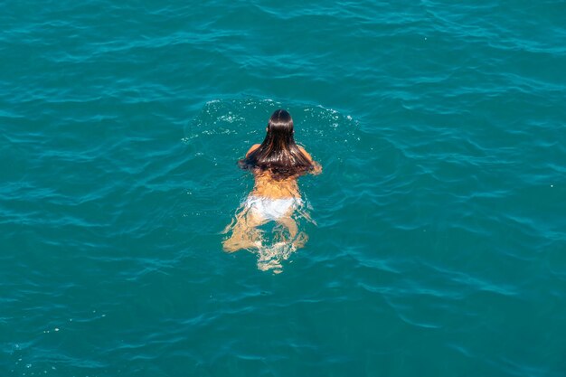 Плавающая девушка в белых купальниках в синем море