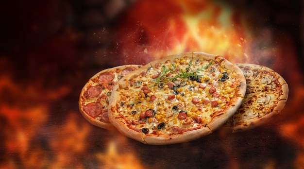 Floating pizzas surrounded by flames in front of a burning oven. Different toppings. sparks and smoke.