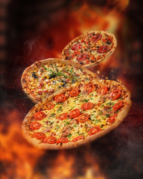 Photo floating pizzas surrounded by flames in front of a burning oven. different toppings. sparks and smoke.