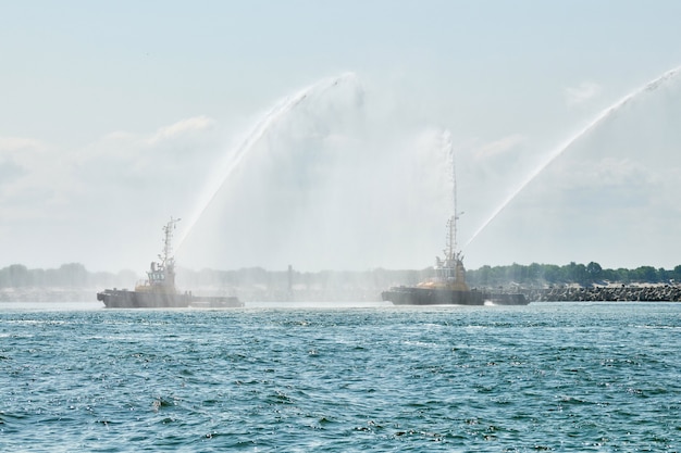 Floating tug boats spraying jets of water, demonstrating\
firefighting water cannons. fire boats spraying foam with fire\
hoses. offshore support vessels testing fire fighting jets