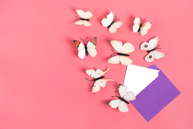 Flock of cabbage butterflies fly out from purple envelope on pink background