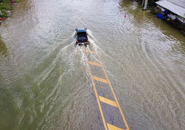 浸水した道路、車が走っている人。空中ドローン写真は、通りが氾濫し、人々の車が通り過ぎ、水をはねかけている様子を示しています。