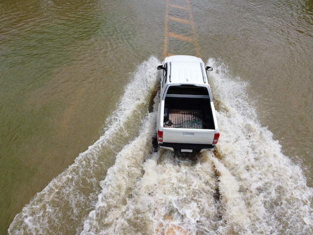 Затопленные дороги, проезжают люди с автомобилями. На фотографии с аэрофотосъемки видно наводнение улиц и проезжающие мимо автомобили с брызгами воды.