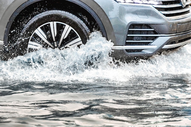 Наводнение в городе после дождя Машина едет по луже под проливным дождем Брызги воды из-под колес автомобиля Транспортный коллапс Суровые погодные условия